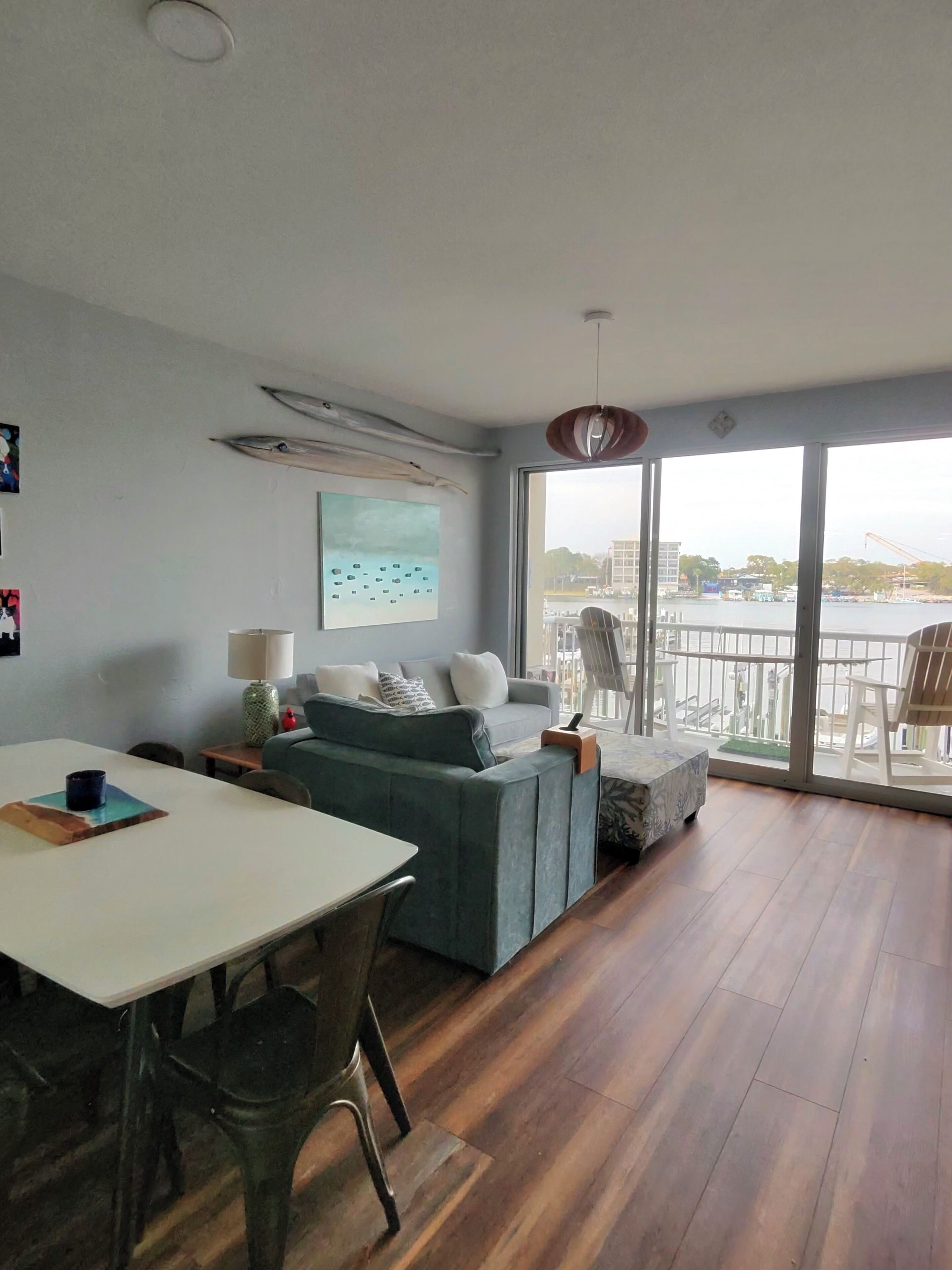 A modern living room with a dining area, a sofa, a table, and a view of a body of water through large windows.