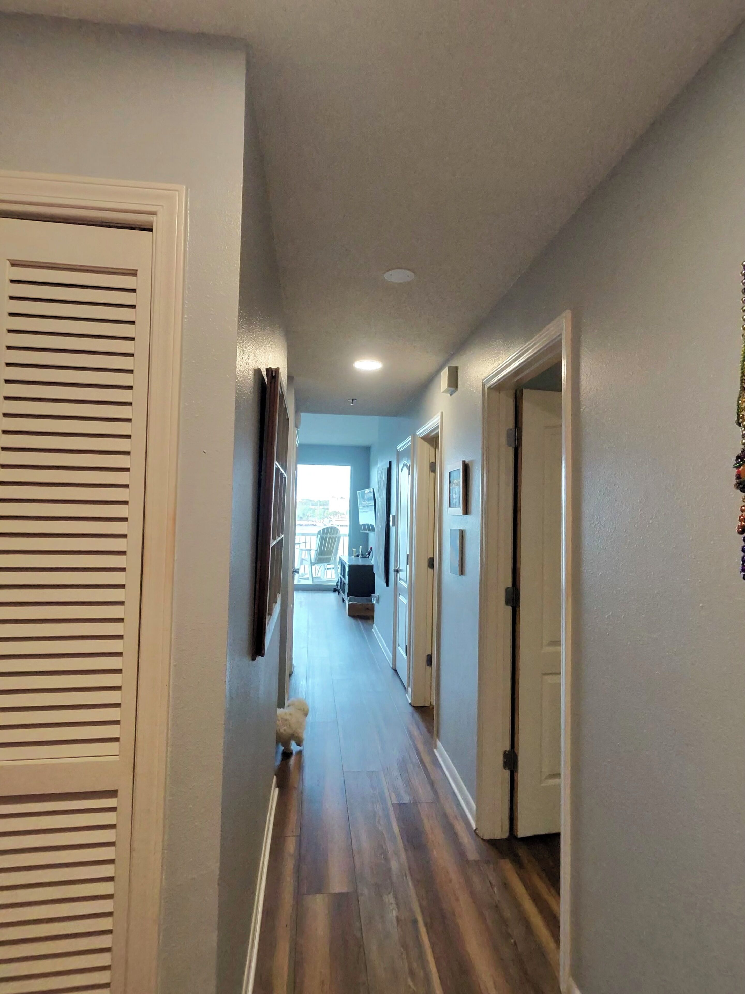 A hallway with wooden flooring, white walls, and doors leading to other rooms.