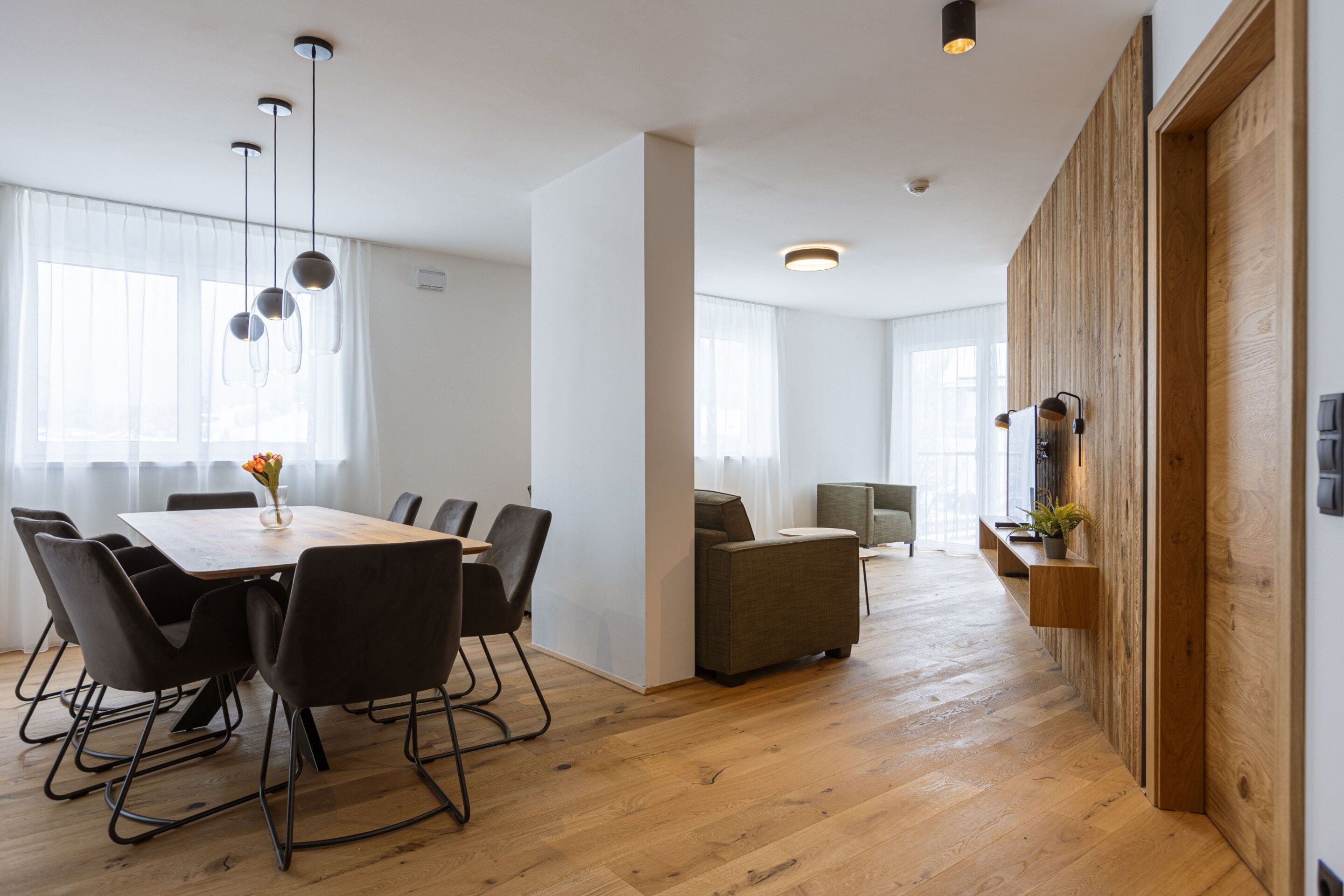 A modern interior with a dining area, sofas, and a wooden accent wall.