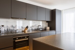 Eine moderne Küche mit dunklen Schränken, einer Edelstahl-Dunstabzugshaube von Bosch, einer Arbeitsplatte aus Granit und einer Spritzschutzwand mit Bergbildern.