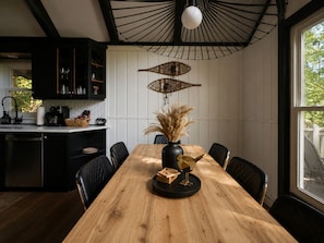 A modern kitchen with a wooden dining table, black chairs, and a unique ceiling light fixture. - 4-bedroom cabin with hot tub, firepit, kids loft, pet friendly. (Beech Mountain)