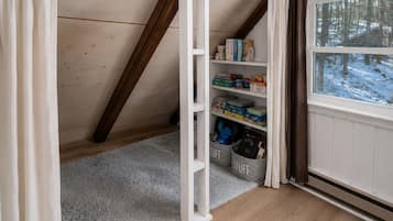 Een kamer met een schuine kap, een raam met uitzicht op een besneeerd landschap, en een plank met diverse spullen.