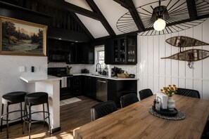 A modern kitchen with black cabinets, a wooden dining table, and a pendant light.