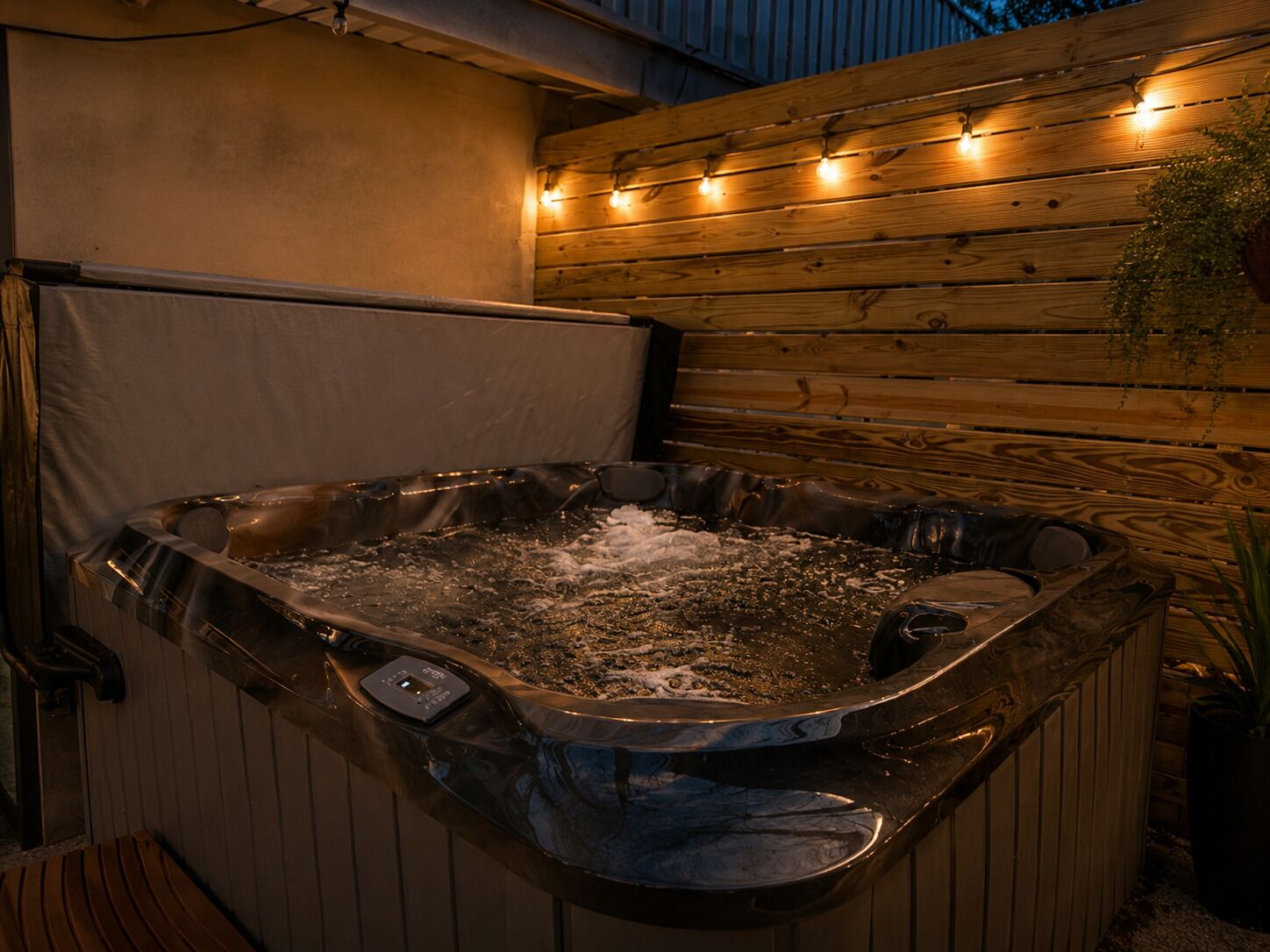 Een hottub met bedieningspaneel, omgeven door houten wanden en lichtslingers.