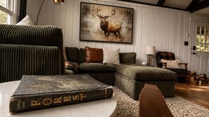 Un salon chaleureux avec un canapé d’angle, une cheminée et un tableau encadré représentant des animaux sauvages.