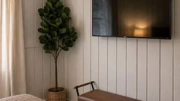 Een hotelkamer met een bed, een bankje, een potplant en een flatscreen televisie aan de muur.