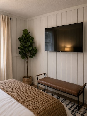 A hotel room with a bed, a bench, a potted plant, and a flat-screen TV mounted on the wall. - 4-bedroom cabin with hot tub, firepit, kids loft, pet friendly. (Beech Mountain)