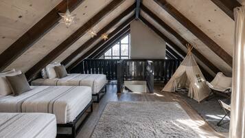 A cozy attic bedroom with two beds, a large window, a wooden ceiling, and a teepee tent.