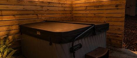 A hot tub with a wooden deck and string lights, surrounded by a wooden fence.