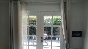 Une pièce avec une porte blanche donnant sur un espace extérieur aménagé avec une table et des chaises. Un panneau est affiché sur le mur, indiquant les consignes à suivre pour les clients.