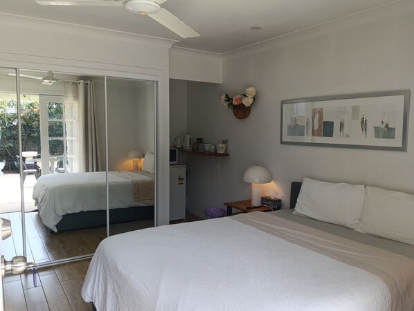 A hotel room with two beds, a ceiling fan, a window with curtains, a bedside table with a lamp, and a wall-mounted picture.