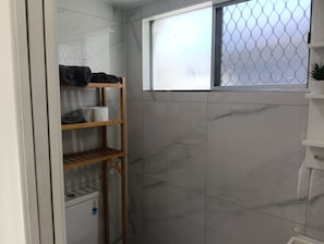 Een badkamer met een marmeren wand, een houten plank met handdoeken en een raam met hor.