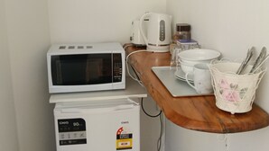 Une petite cuisine équipée d’un four à micro-ondes, d’un petit réfrigérateur, d’une bouilloire et d’une machine à café, le tout installé sur un plan de travail en bois.