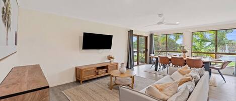 A modern living room with a flat-screen TV, a wooden console, a sofa, and a dining area with a table and chairs.