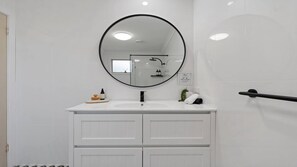 A bathroom with a white vanity, a round mirror, and a glass shower enclosure.