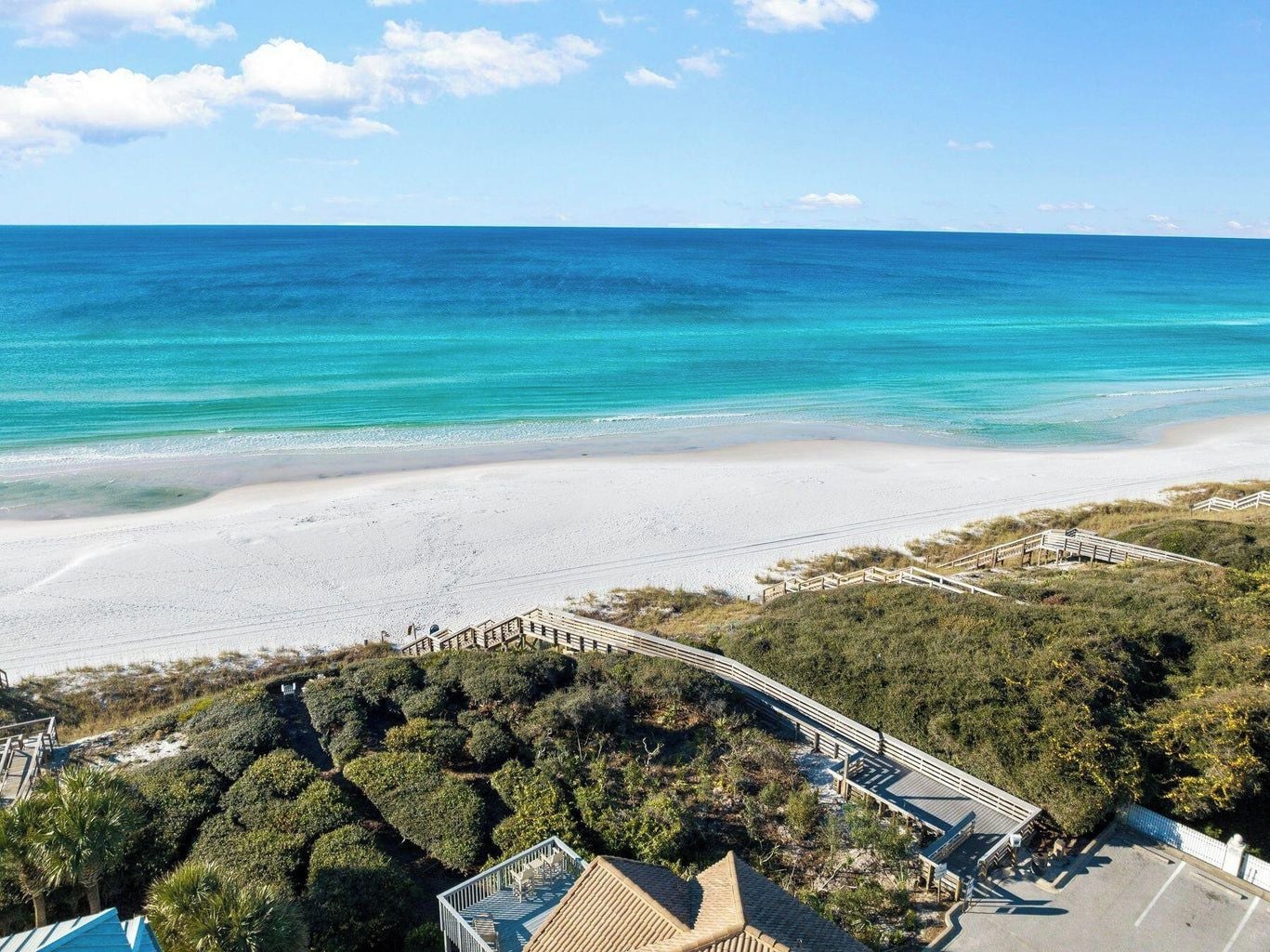 A beach with a wooden boardwalk leading to a building with a pool.