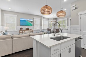 A modern kitchen with a central island, white cabinetry, and a built-in sink. - Bluegrass by the Sea | Golf Cart | 6 Bikes | Corner Lot | 2 King Suites | Near Seaside (Santa Rosa Beach)