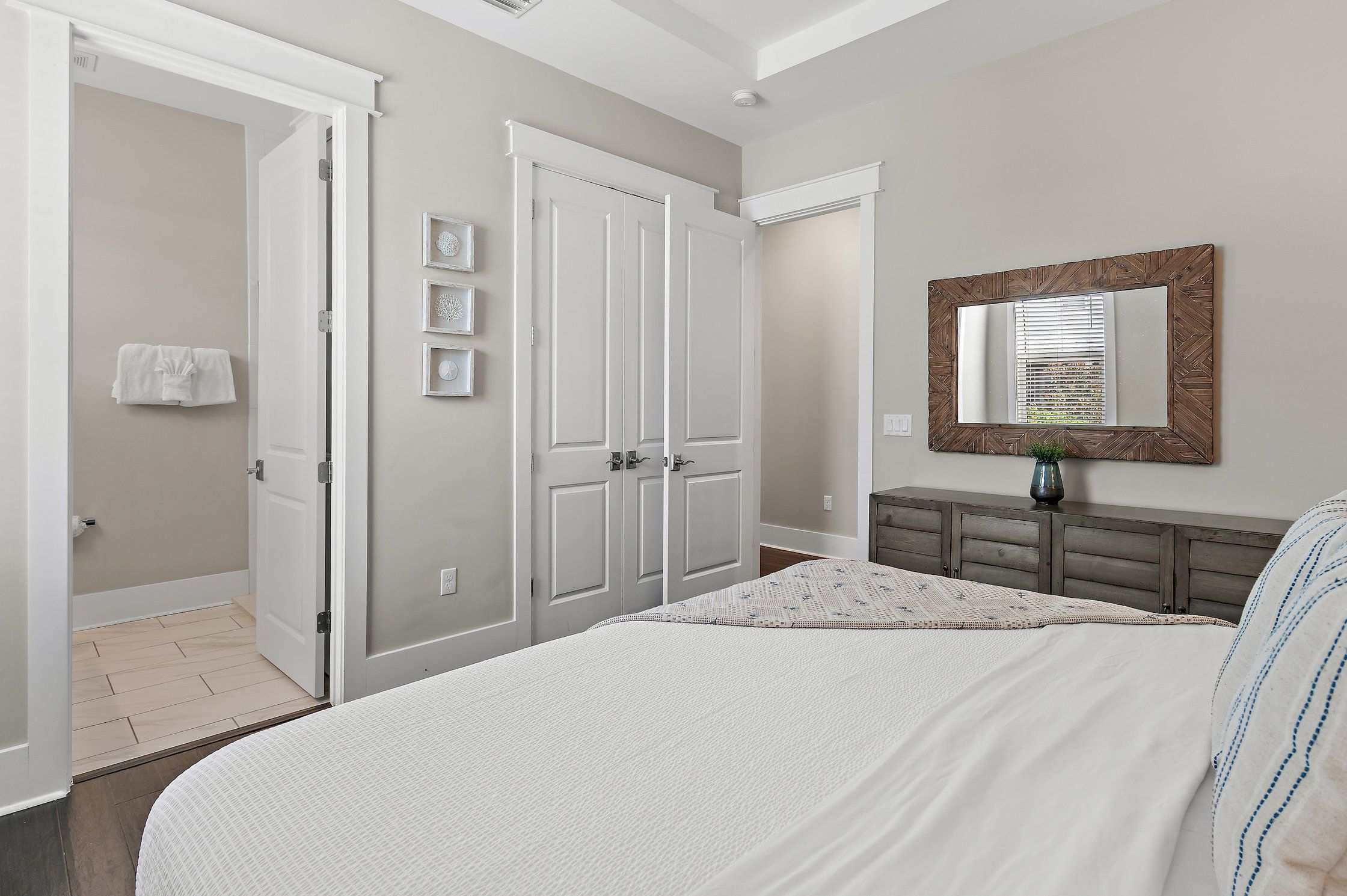 A bedroom with a large bed, a dresser, a mirror, and a door leading to another room.