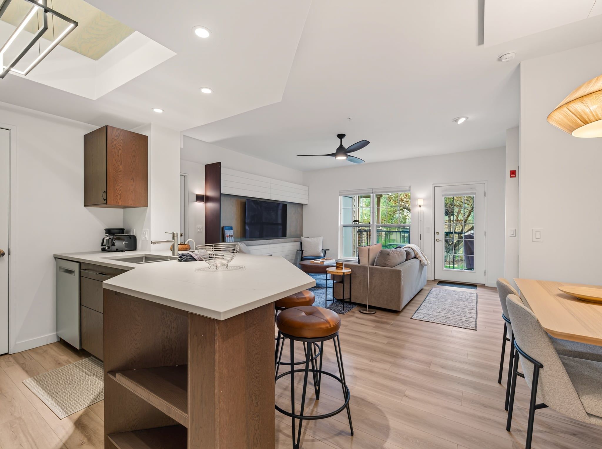 Una cocina moderna con una isla central, taburetes de bar y una zona de comedor con mesa de madera.
