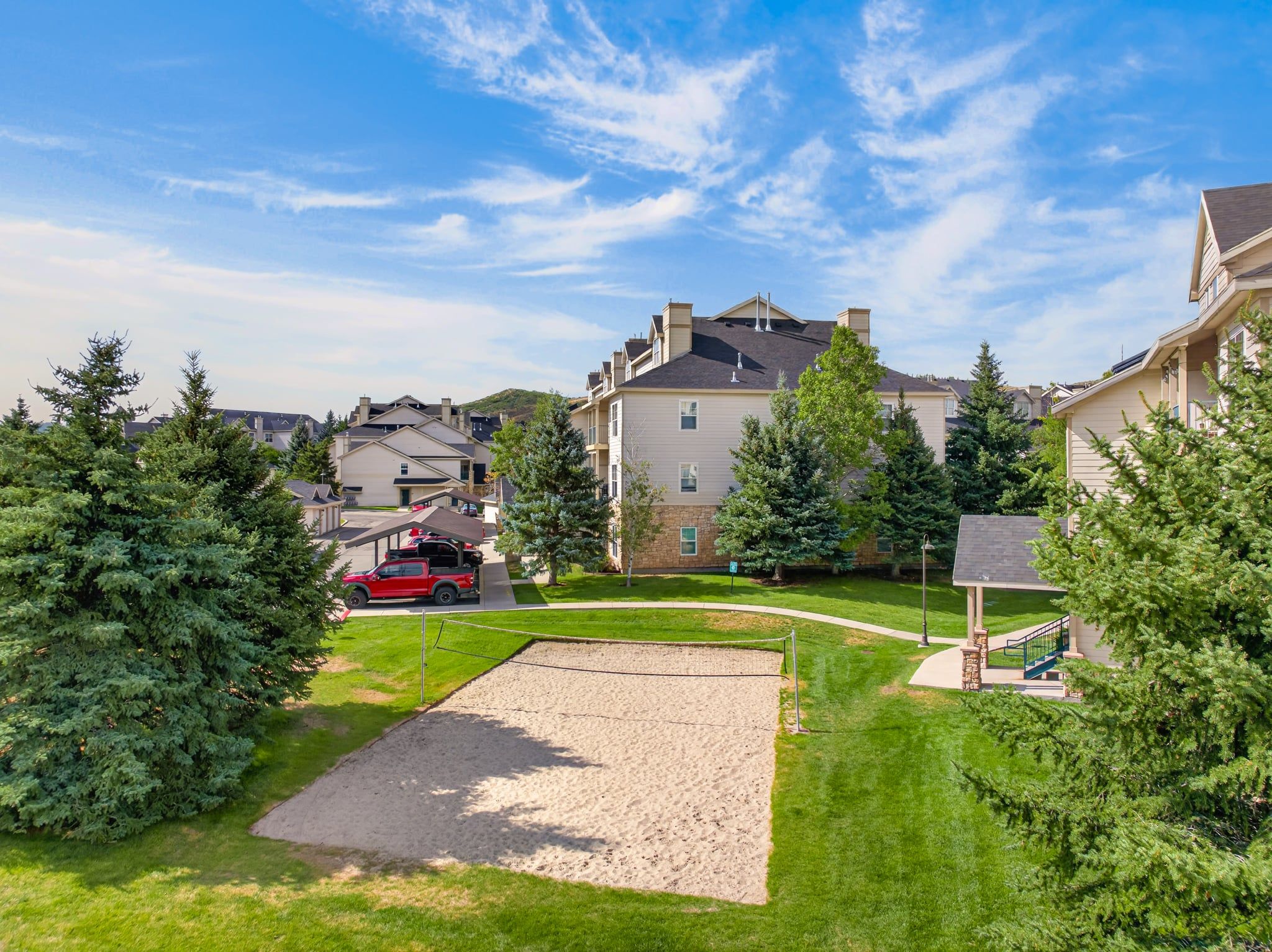 A residential area with houses, a red vehicle, and a sandy play area.