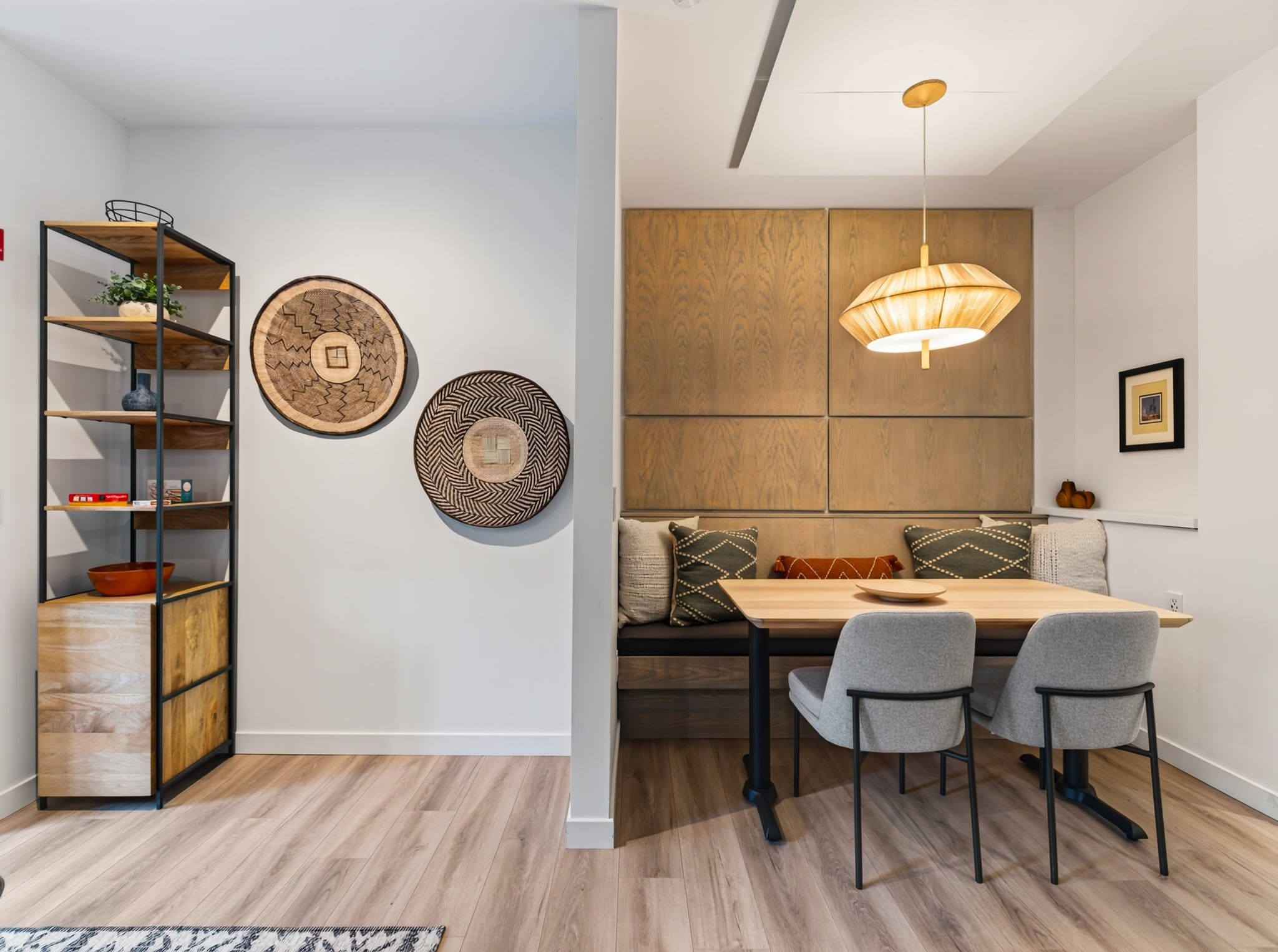 Un comedor con mesa de madera, dos sillas, un banco con cojines e iluminación colgante.