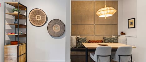 A dining area with a wooden table, two chairs, a bench with cushions, and a hanging pendant light.