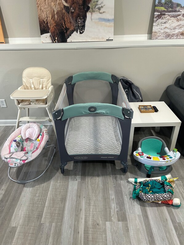 A room with a baby play area including a high chair, a baby rocker, and a baby bed.