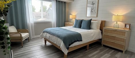 Un dormitorio con cama, mesitas de noche, ventilador de techo, ventana con cortinas y una lámpara de pared.