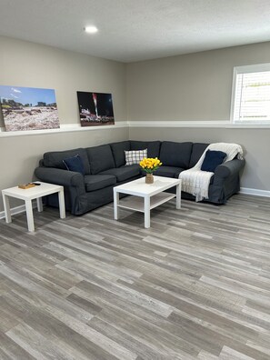 A living room with a grey sectional sofa, two white side tables, and a vase with yellow flowers.