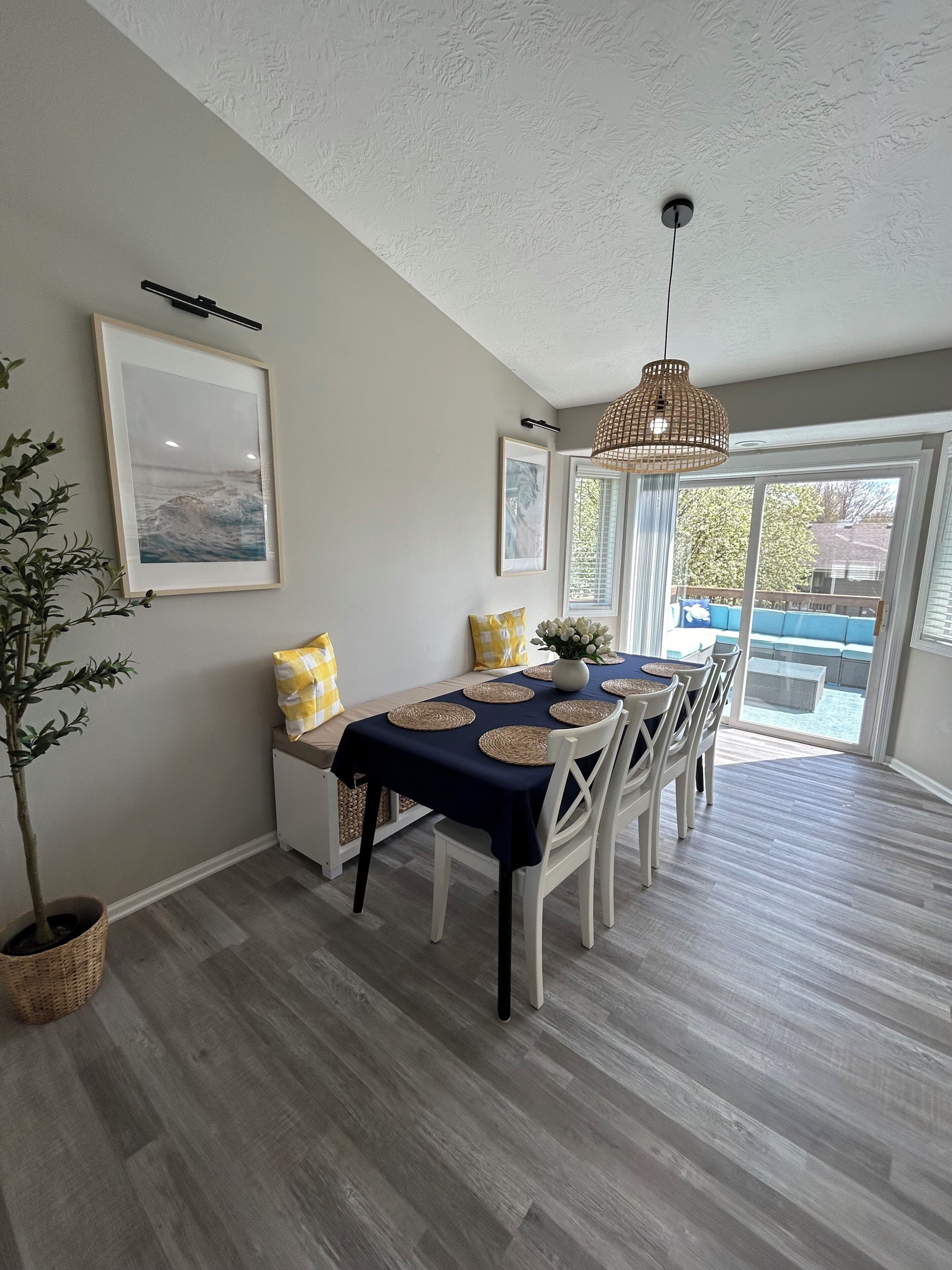 Comedor con una mesa dispuesta para cuatro, una lámpara colgante y vistas a un área de estar exterior a través de un ventanal.