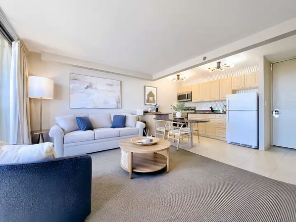 A modern living room with a sofa, coffee table, and a dining area with chairs. There is a kitchen with cabinets and a refrigerator. - 21F-Beautiful Waikiki-1BR Condo-Near Beach w/ Diamond Head & Partial Ocean Views (Honolulu)