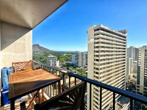 A balcony with a wooden table and chairs, overlooking a cityscape with high-rise buildings and a mountain in the distance. - 21F-Beautiful Waikiki-1BR Condo-Near Beach w/ Diamond Head & Partial Ocean Views (Honolulu)