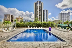 A swimming pool with lounge chairs, surrounded by palm trees and buildings. - 21F-Beautiful Waikiki-1BR Condo-Near Beach w/ Diamond Head & Partial Ocean Views (Honolulu)