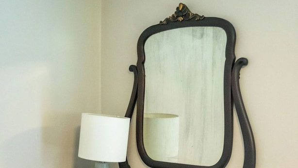 Un aparador de madera oscura con un espejo y una lámpara blanca junto a una pared.
