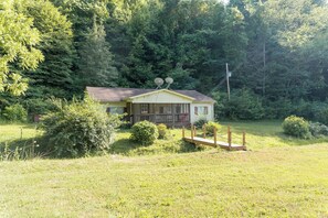 Ein kleines Haus mit Veranda, umgeben von einer Wiese und dichtem Wald.