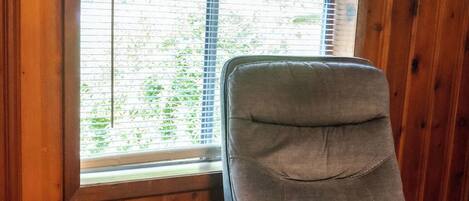 Una habitación con un revestimiento de madera, una ventana con persianas y un sillón tapizado en gris.