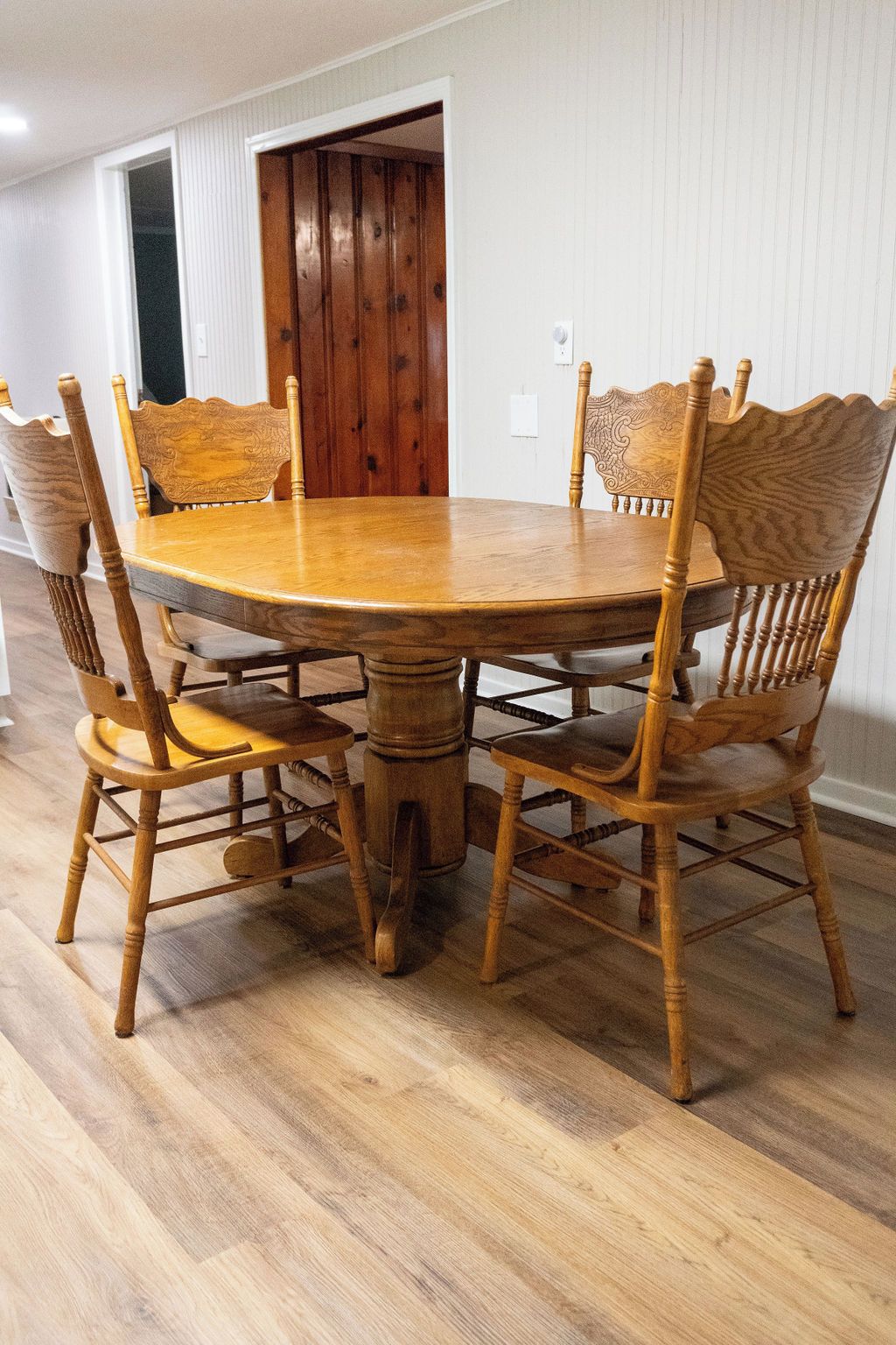 Una mesa de comedor con seis sillas, piso de madera y una puerta al fondo.