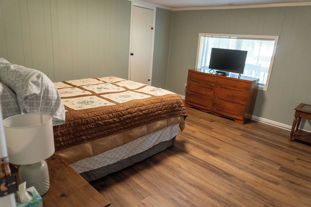 Un dormitorio con cama, cómoda, televisor y ventana.