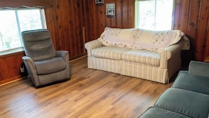 Una habitación con piso de madera, un sofá a rayas, un sillón gris y un sofá verde.