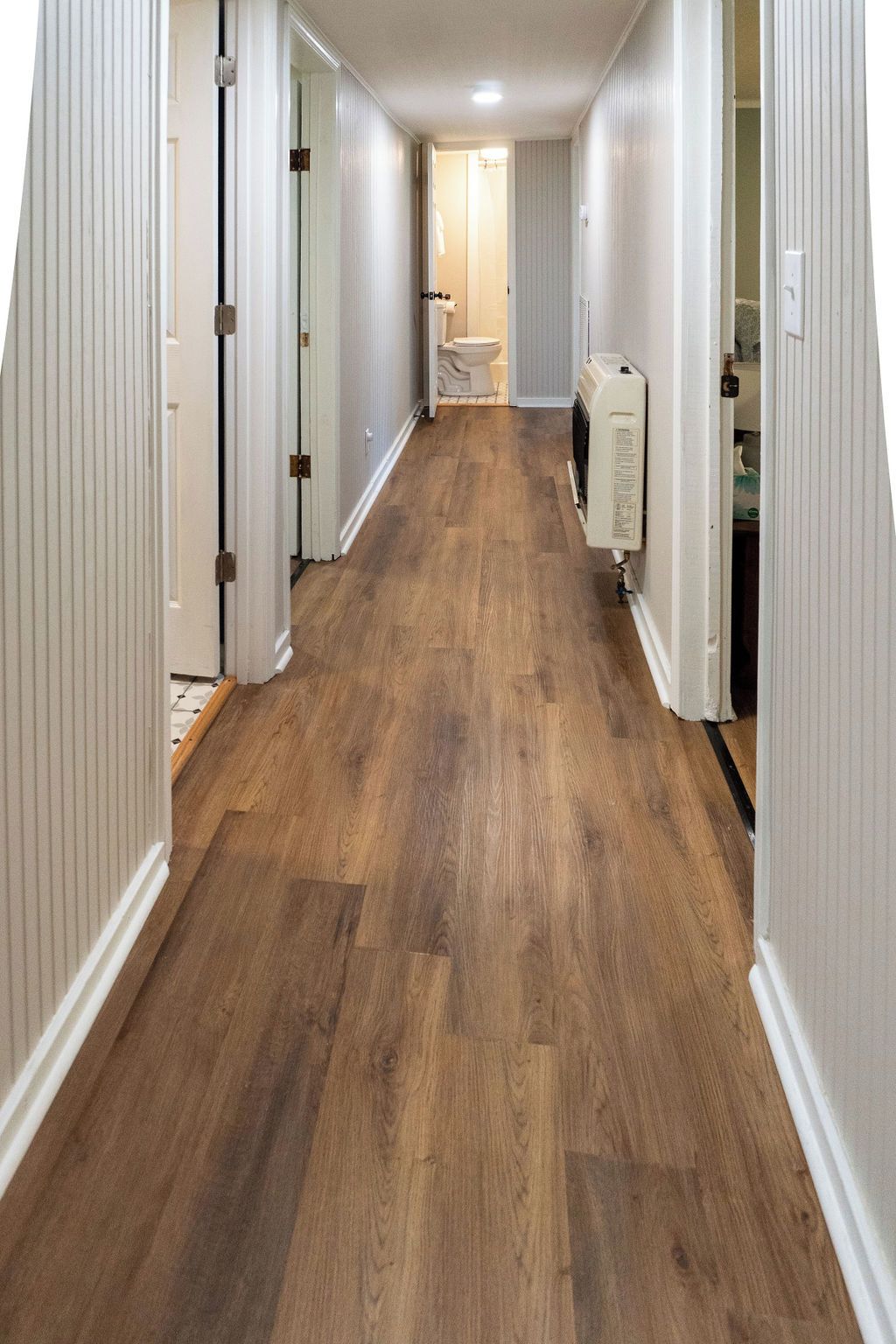 A hallway with wooden flooring, white walls, and doors leading to rooms.