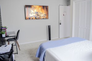 Ein Schlafzimmer mit einem Bett, einem Schreibtisch mit Stuhl, einem Heizlüfter und einer Tür mit Schloss.