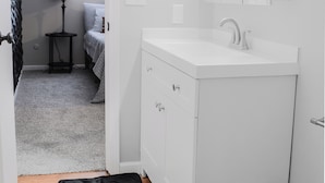 A white bathroom with a sink, mirror, and cabinets. There is a black rug on the floor and a pink trash bag. - Serene Tuxedo 3-bedroom townhome with AC in charming Grandview (Grandview)
