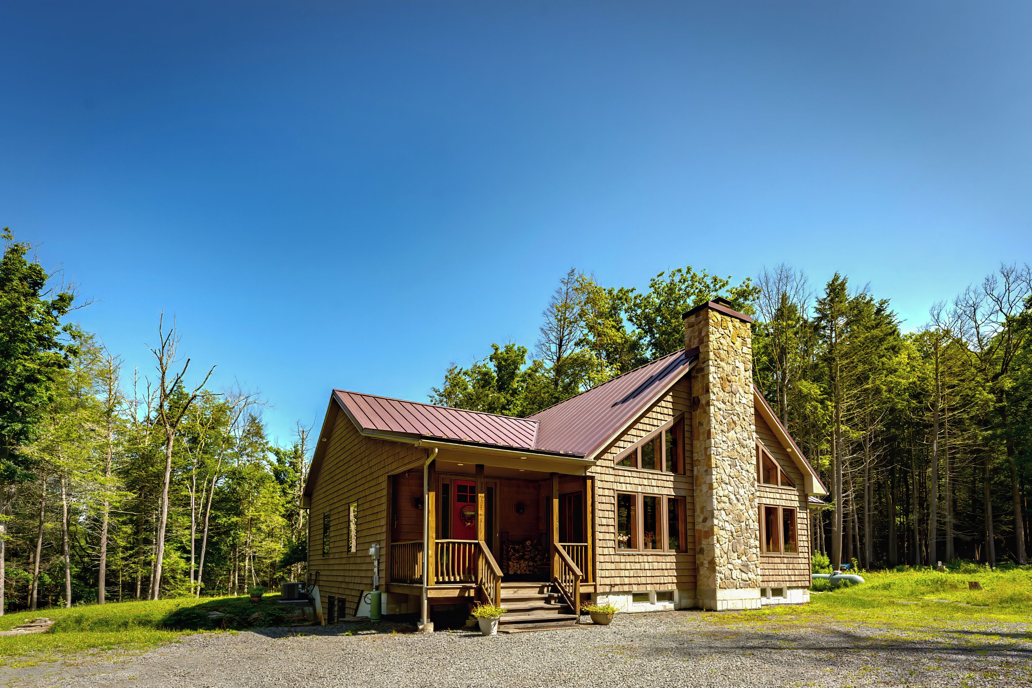 Une cabane en rondins avec un porche, une cheminée en pierre et une forêt en arrière-plan.