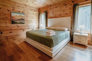 A wooden-paneled bedroom with a bed, a nightstand, and a painting on the wall.