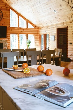 Interior de uma cabana de madeira com uma mesa de jantar, cadeiras e uma revista sobre a mesa.
