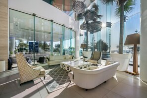 A modern lobby with a glass wall, white furniture, and a view of the outdoors. - Halo by Aryve | Surfers Paradise (Surfers Paradise)
