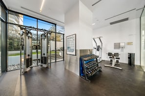 Ein Fitnessstudio mit verschiedenen Trainingsgeräten, darunter Kraftmaschinen und Kurzhanteln, und einem großen Fenster mit Blick ins Freie.
