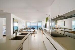 A modern kitchen with a central island, a dining area with a view, and a living space with a large window overlooking the ocean. - Halo by Aryve | Surfers Paradise (Surfers Paradise)