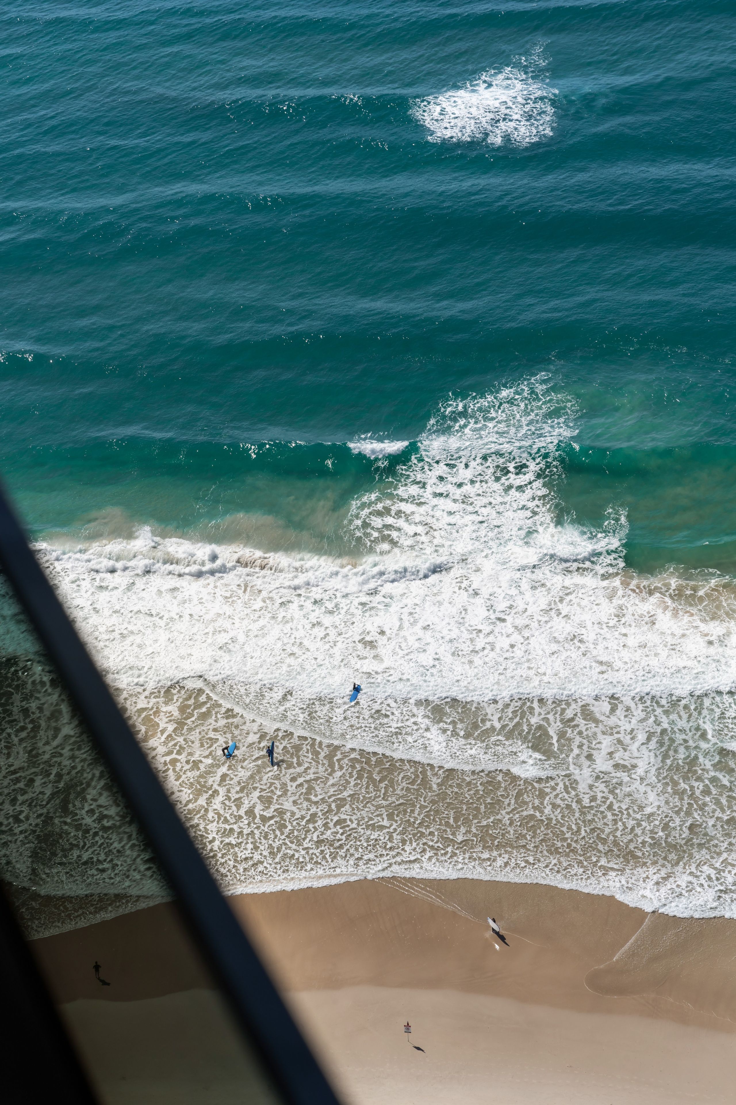 Una playa con olas rompiendo en la orilla, cielo despejado y algunas personas en el agua.