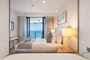 Habitació d'hotel amb un llit gran, un bany amb banyera, una finestra amb vista al mar i un quadre a la paret.